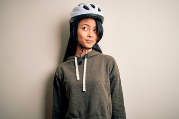 Young beautiful chinese woman wearing bike helmet over isolated white background smiling looking to the side and staring away thinking.