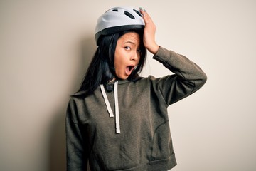 Young beautiful chinese woman wearing bike helmet over isolated white background surprised with hand on head for mistake, remember error. Forgot, bad memory concept.