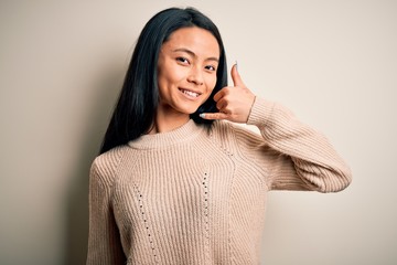 Young beautiful chinese woman wearing casual sweater over isolated white background smiling doing phone gesture with hand and fingers like talking on the telephone. Communicating concepts.