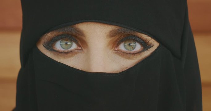 Portrait of a muslim woman wearing traditional black niqab showing only her green eyes, middle east culture