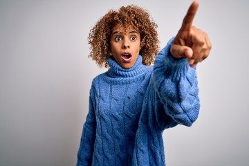 Young beautiful african american woman wearing turtleneck sweater over white background Pointing with finger surprised ahead, open mouth amazed expression, something on the front