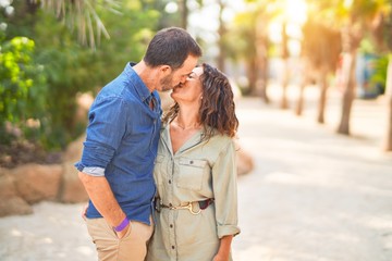 Fototapeta premium Middle age beautiful couple smiling happy and confident at town park. Standing with smile on face hugging and kissing