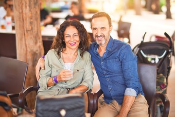 Middle age beautiful couple smiling happy and confident at town park. Sitting on chair with smile on face hugging