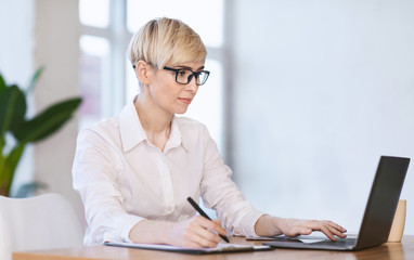 Businesswoman Working On Laptop Taking Notes Sitting In Modern Office