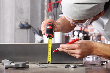 man work in home workshop garage measure metal with tape meter and use pencil, on the workbench with wrenches and hammer, diy and craft concept