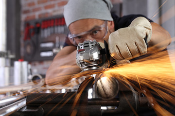 man work in home workshop garage with angle grinder, goggles and construction gloves, sanding metal makes sparks closeup, diy and craft concept