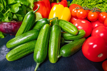 Fresh vegetables on dark background. On the table are cucumbers, tomatoes and peppers. Ingredients for fresh salad. Vegetarianism. A raw food diet. Vegetables contain vitamins.