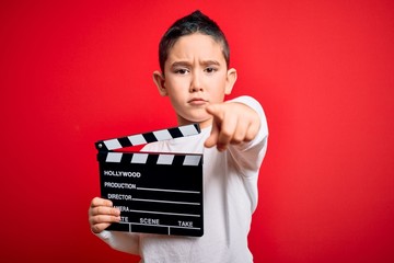 Young little boy kid filming video holding cinema director clapboard over isolated red background...