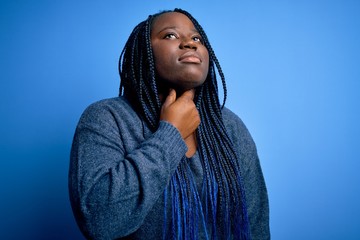 African american plus size woman with braids wearing casual sweater over blue background Touching painful neck, sore throat for flu, clod and infection