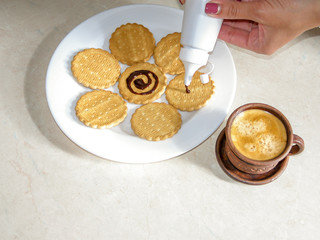 Chocolate decorated cookies laid out on a white plate. A cup of coffee.