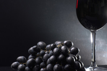 A glass of red wine next to grapes on a dark background. Close-up.