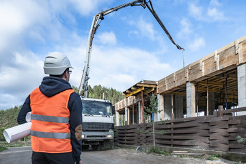 Fototapeta premium A man watches the pouring of concrete on a construction site. Construction of a country house. A person controls the pouring of concrete. Housing construction. A cement mixer pours cement.