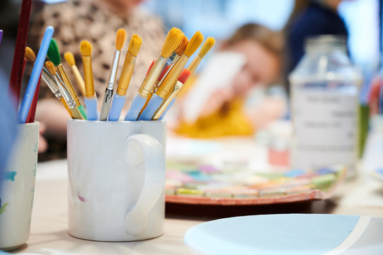 Bunte Pinsel mit gelben Borsten stehen in einer Kaffeetasse auf dem Tisch einer Kunstschule