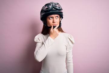 Young beautiful motorcyclist woman with blue eyes wearing moto helmet over pink background Thinking worried about a question, concerned and nervous with hand on chin