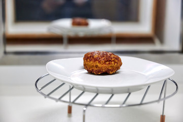 Eine Frikadelle auf einem weißen Teller hinter einer Scheibe eines Schaufensters