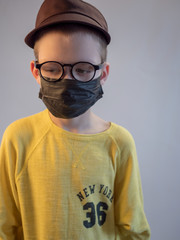cute blonde boy in black medical mask and glasses is quarantined at home. child coughs heavily and wears mask. concept of fight against the coronavirus epidemic and proper prevention of infections