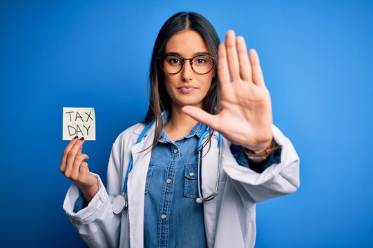 Young Doctor Woman Wearing Stethoscope Holding Paper With Tax Day Message With Open Hand Doing Stop Sign With Serious And Confident Expression, Defense Gesture