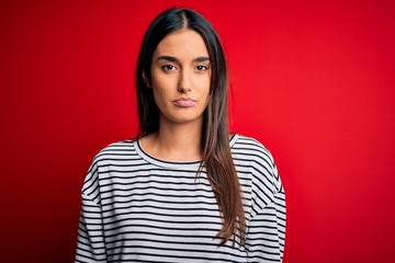 Fototapeta premium Young beautiful brunette woman wearing casual striped t-shirt over red background depressed and worry for distress, crying angry and afraid. Sad expression.