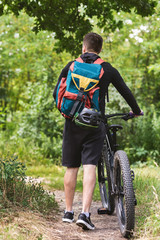 Back view of guy backpacking with bike in forest