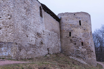 The ruines of old ancient medieval fortress or castle with turret or tower and brick, cobble or stone wall in the cloudy spring or autumn day © Майджи Владимир