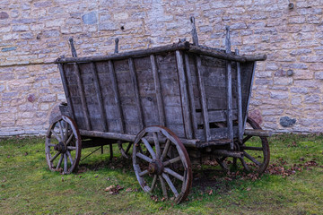 The broken ancient medieval rural wood cart or wagon on the green grass on the background of the castle or fortress stone or brick wall 