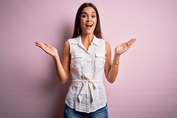 Young beautiful brunette woman wearing casual shirt standing over pink background celebrating crazy and amazed for success with arms raised and open eyes screaming excited. Winner concept