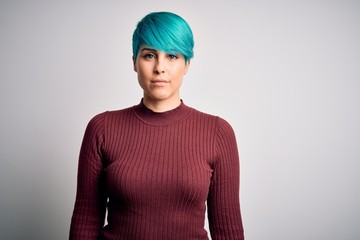 Young beautiful woman with blue fashion hair wearing casual sweater over white background with serious expression on face. Simple and natural looking at the camera.