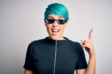 Young woman with blue fashion hair wearing thug life sunglasses over white background pointing finger up with successful idea. Exited and happy. Number one.