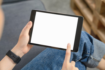 Close-up of hand holding black tablet on sofa in living room.
