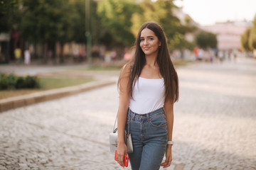 Attractive young woman walking in centre of city in summer time. Beautiful brunette in white shirt. Smile