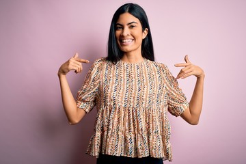 Young beautiful hispanic fashion woman wearing elegant style over pink background looking confident...