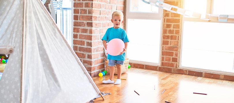 Young caucasian kid playing at kindergarten with toys. Preschooler boy happy at playroom.