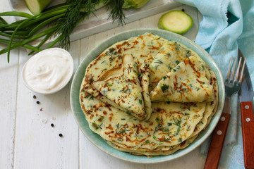 Snack or summer lunch. Zucchini pancakes with greens served with sour cream on a wooden table. Copy space.