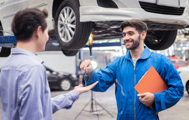Mechanic holding clipboard giving the key back to car owner in the workshop garage. Car auto...