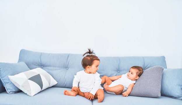 Beautiful infant happy girls playing together at home kindergarten sitting on the sofa