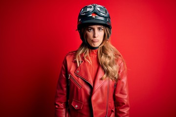 Young beautiful brunette motrocyclist woman wearing moto helmet over red background depressed and worry for distress, crying angry and afraid. Sad expression.