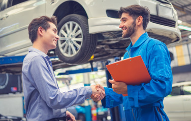 Mechanic holding clipboard shaking hands with car owner in the workshop garage. Car auto services concepts