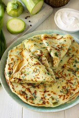 Summer lunch or Snack. Zucchini pancakes with greens served with sour cream on a wooden table.