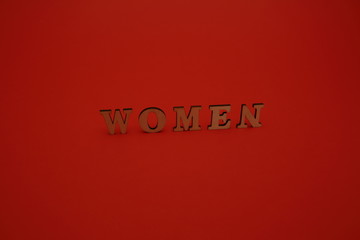 Word WOMEN mand of wooden letters standing a bit aslant isolated on red background
