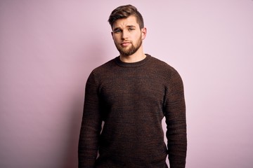 Obraz premium Young blond man with beard and blue eyes wearing casual sweater over pink background Relaxed with serious expression on face. Simple and natural looking at the camera.