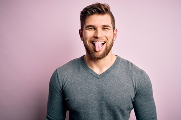 Obraz premium Young handsome blond man with beard and blue eyes wearing casual sweater sticking tongue out happy with funny expression. Emotion concept.