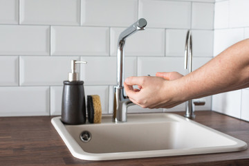 Hand washing underwater from a faucet in the kitchen. leanliness, water saving, washing dishes in a bright Scandinavian interior