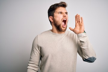 Young handsome blond man with beard and blue eyes wearing casual sweater shouting and screaming loud to side with hand on mouth. Communication concept.