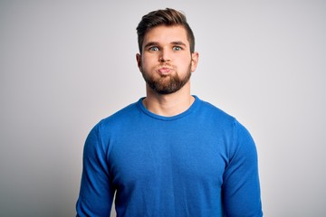 Young handsome blond man with beard and blue eyes wearing casual sweater puffing cheeks with funny face. Mouth inflated with air, crazy expression. - obrazy, fototapety, plakaty