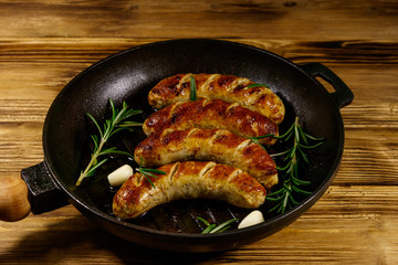 Fried sausages with rosemary, garlic and spices in cast iron grill frying pan on wooden table