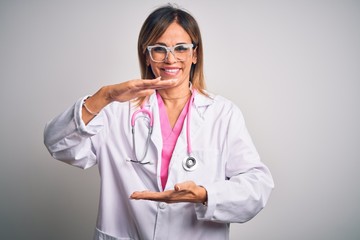 Middle age beautiful doctor woman wearing pink stethoscope over isolated white background gesturing with hands showing big and large size sign, measure symbol. Smiling looking at the camera. Measuring