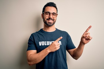 Handsome man with beard wearing t-shirt with volunteer message over white background smiling and looking at the camera pointing with two hands and fingers to the side.