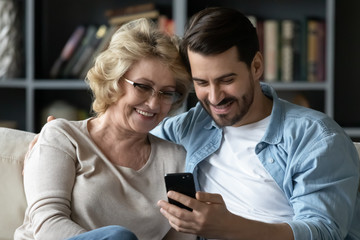 Smiling senior mom and adult son using smartphone together