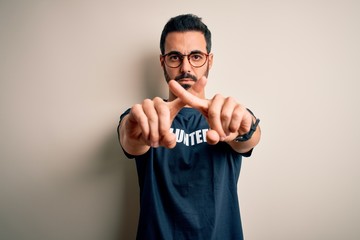 Handsome man with beard wearing t-shirt with volunteer message over white background Rejection expression crossing fingers doing negative sign