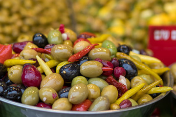 A pile of pickled olives from different varieties. Mix with hot peppers, in a metal bowl. Blurred background. Arabic style. The Old Market, Jerusalem.